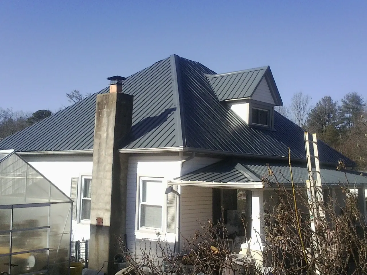 Dark blue standing seam metal roof on a white farmhouse with dormer — Slate & Tile Roof Repair by Roofing Brothers in High Ridge