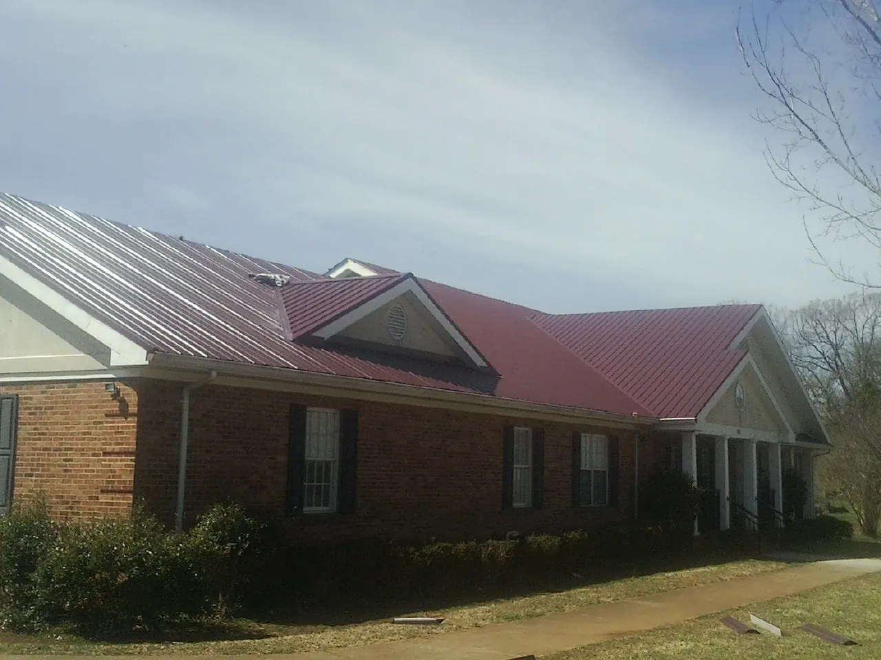 Red metal roof with gabled entries on a long brick building, from a Hail Damage Roof Repair job in High Ridge