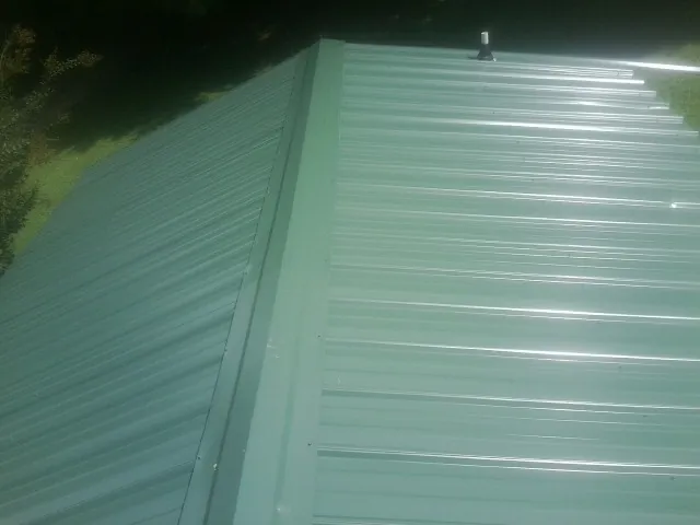 New green metal panels meeting at the ridge of a roof — Flat Roof Repair work by our crew in High Ridge