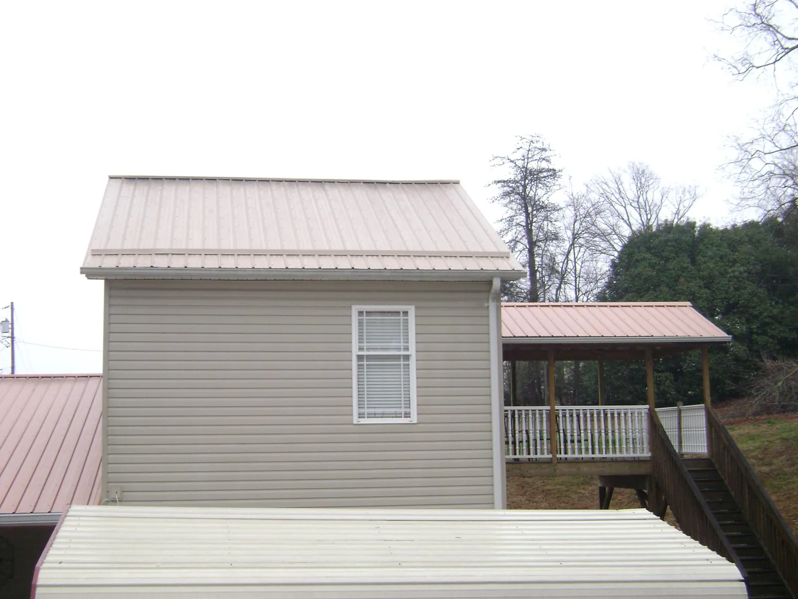 Tan metal roofs on a two story addition and attached porch, from a Roof Replacement job in High Ridge